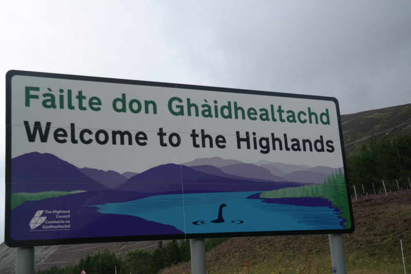 Road sign welcoming visitors to the Highlands. Someone has added a hand-drawn Nessie into the loch.